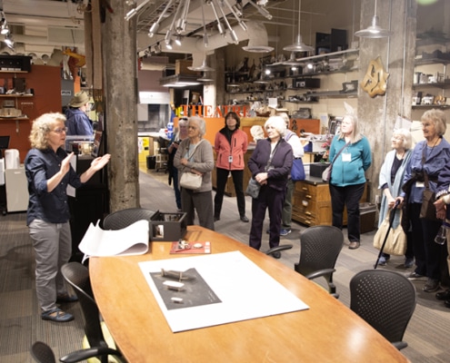 Group of tour participants standing around a working table inside a studio.